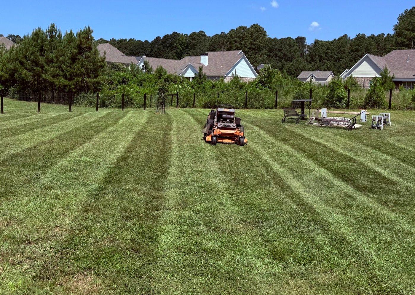 Orange zero-turn mower laying fresh stripes across a wide green lawn in Covington by Kaus Cuts